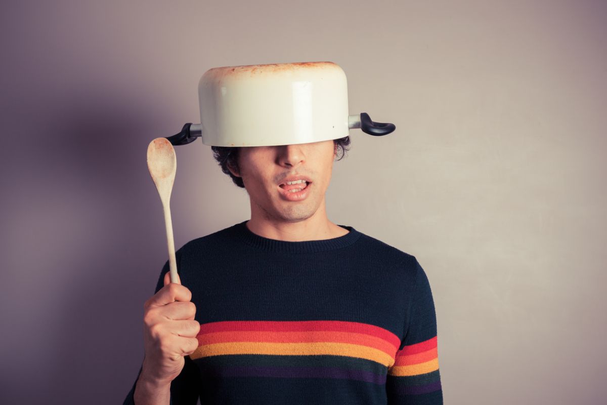 Man wearing a cooking pot as a helmet and holding a wooden spoon, symbolizing foolish or reckless financial behavior and speculative decision-making.