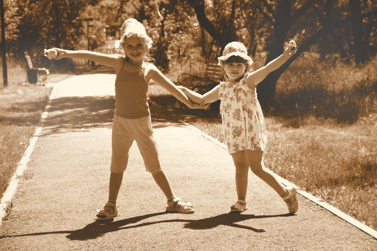 Sepia-toned photograph of two children holding hands and smiling on a path, evoking nostalgia, childhood memories, and reflections on the emotional value of the past.